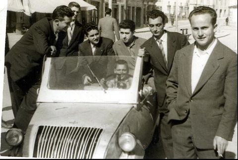 Un grupo de personas posan divertidas alrededor de un Biscuter, en la plaza de Santa Ana de Chantada, en 1960