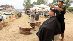 Richard Lage atendiendo a un cliente en su peluquera porttil en el chiringuito Kenia, en la playa de Area, en Viveiro