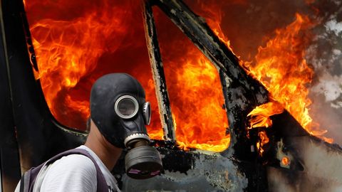Un manifestante, con una m�scara de gas, junto a una furgoneta en llamas durante las violentas protestas contra las medidas de austeridad en Atenas.