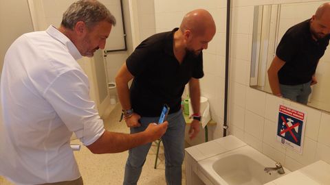 Los socialistas Marcos Rey e Iv&aacute;n Puentes, en uno de los ba&ntilde;os del CEIP Santo Andr&eacute; de Xeve, donde una se&ntilde;al advierte de que el agua no es potable