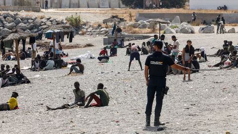 Un agente de polic&iacute;a patrulla en playa del Trampol&iacute;n mientras los migrantes esperan para entrar en un centro de acogida de migrantes de corta estancia (CETI). 