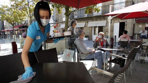 Una camarera limpia una mesa en una terraza de la calle Cardenal de Monforte, abierta hoy por primera vez en dos meses