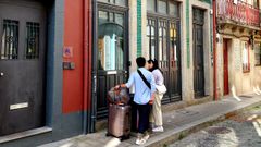 Dos viajeros en una calle de Oporto, junto a la entrada de un piso turstico.