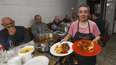 Montse Carballeira llevando platos, con clientes sentados junto a la cocina de le�a 