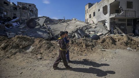 Dos ni�os palestinos pasan junto a casas destruidas tras la operaci�n militar israel� en el campo de refugiados de Al Maghazi.