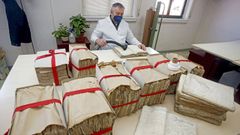 Un operario limpia el polvo de varios legajos