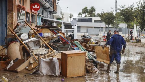 Varias personas quitan el barro de las calles mientras se acumula el mobiliario que han tenido que sacar debido a las inundaciones por las fuertes lluvias