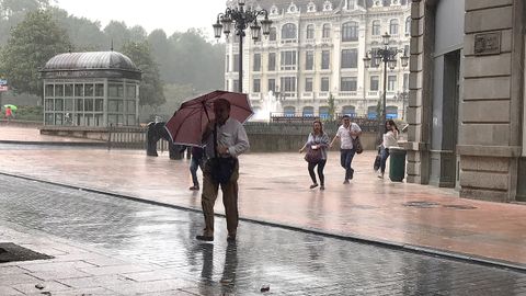 Los peatones se protegen de las lluviosas tormentas de verano que cayeron sobre Oviedo