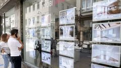 Personas mirando ofertas de pisos en el escaparate de una inmobiliaria.