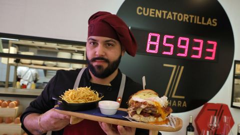 Un cocinero del restaurante Zahara, en Ferrol, muestra una hamburguesa de la carta, con el contador de tortillas de fondo.