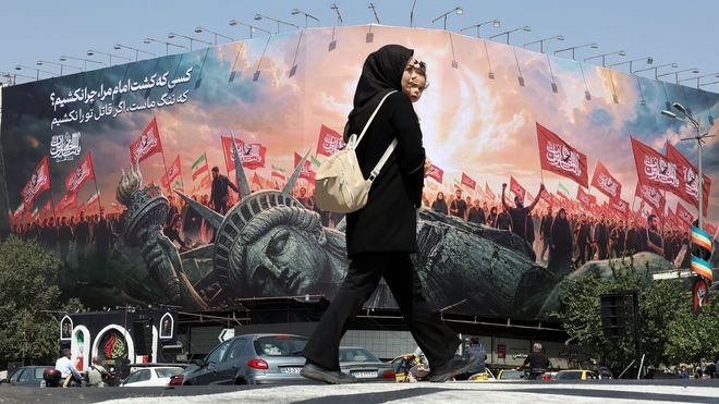 Una mujer pasea frente a un mural con propaganda proiran� y antiamericana.
