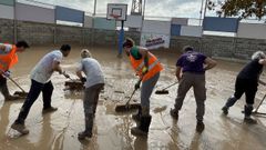 Varios voluntarios trabajan para limpiar el barro de la cancha de baloncesto del colegio de Horno Alcedo.