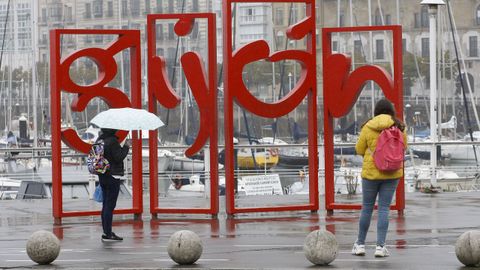 Paseantes se protegen de la lluvia en Gij�n