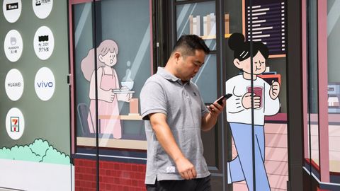 Un hombre camina revisando su m&oacute;vil en una zona comercial de Pek&iacute;n.