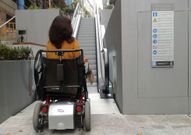 Una joven en silla de ruedas junto al cartel que especifica los usos. 