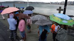 Turistas bajo los paraguas en la Iglesia de San Pedro en la playa de San Lorenzo, en Gij�n