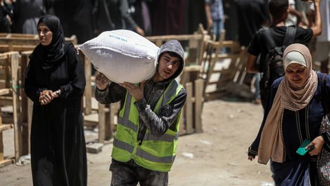 Palestinos llevan bolsas de harina mientras otros esperan frente a un punto de distribuci�n establecido por el Programa Mundial de Alimentos (PMA) de las Naciones Unidas en la ciudad de Gaza.