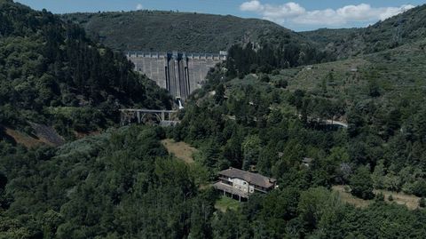 La edificación principal destaca entre los árboles, con el embalse de O Bao al fondo.