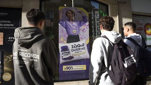 Adolescentes frente a una farmacia con un cartel publicitario de productos para dormir