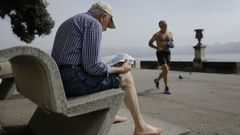 Un hombre leyendo el peridico descalzo este domingo mientras otro corre sin camiseta por el paseo martimo de A Corua con algo de niebla