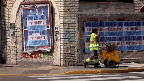 Una trabajadora pasa frente a unos carteles de Milei antes de su investidura.