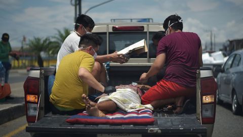 Varios hombres protegidos con mascarillas trasladan a un enfermo en la parte de atrs de una camioneta en Duran, Ecuador