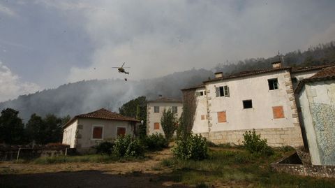 Un helcptero echa agua cerca de las casas del poblado de A Chaira