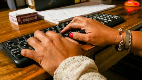 Unas manos de mujer escriben en el teclado de un ordenador, sobre una mesa de madera