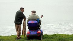Dos personas mayores conversan frente al mar en Boiro