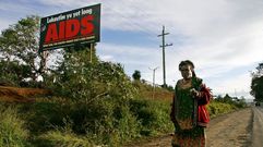 Una mujer camina descalza sobre el asfalto en Pap�a Nueva Guinea; en el fondo, un cartel que alerta de la amenaza del virus del SIDA.