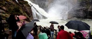Los turistas se acercaron a la cascada de O zaro incluso bajo la lluvia, atrados por su elevado caudal.
