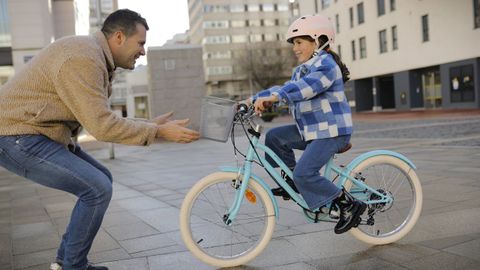 Ni�a montando en bicicleta mientras su padres la espera orgulloso