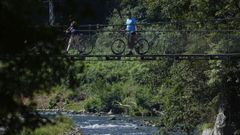 Unos ciclistas pasan por una pasarela sobre el ro Nalnen en Las Caldas (Asturias)