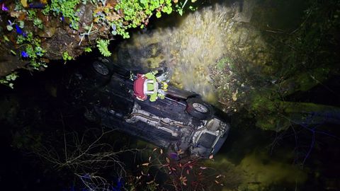 Un bombero del parque comarcal trabajando sobre el turismo volcado en el agua