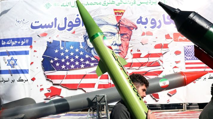 Un hombre porta un misil simulado frente a una pintada contra Trump en una calle de Teher�n