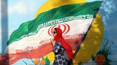 Una mujer iran pasa frente a un mural con la bandera del pas.