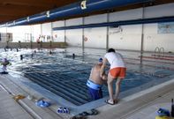 Un monitor ayuda a un usuario de la piscina ayer por la tarde con numerosos abonados al fondo. 