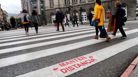 Varias personas cruzan un pase de peatones con un aviso de recomendacin de distanciamiento social pintado por el Ayuntamiento de Oviedo como forma de frenar la pandemia del coronavirus.