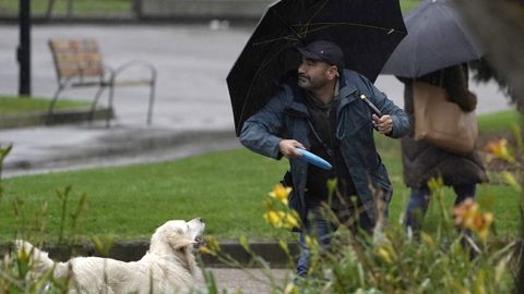 Un hombre se dispone a lanzar un frisbee a su perro esta maana bajo la lluvia en Oviedo.