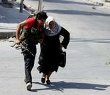 Un joven ayuda a una mujer en medio de combates en Alepo.