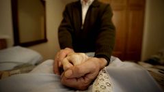 Un cuidador sostiene la mano de su mujer encamada