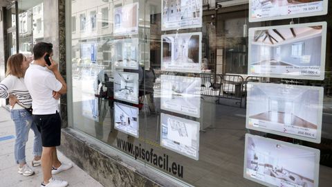 Dos personas mirando ofertas de pisos en el escaparate de una inmobiliaria de Lugo