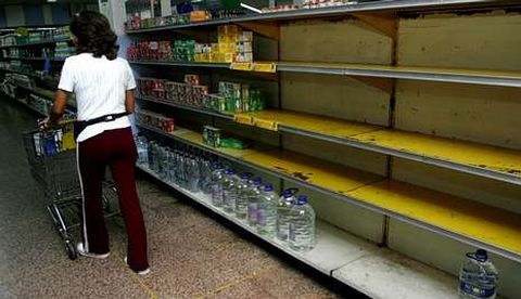 Una mujer pasa por el pasillo de un supermercado que tiene las estanteras medio vacas.