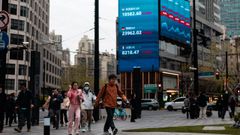 Varias personas caminan por una calle de Shanghai bajo una gran pantalla que muestra los &uacute;ltimos datos burs&aacute;tiles.