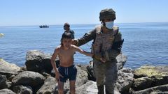 Un militar espa�ol ayuda a un menor migrante a salir del agua en la playa del Tarajal
