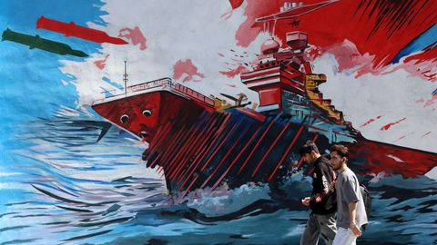 Dos personas caminan en Teher�n ante un mural que muestra un ataque a un buque de guerra de Estados Unidos.