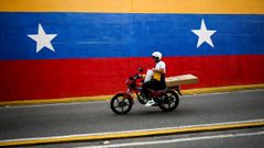 Un motorista pasa por un mural cunha bandeira de Venezuela. 