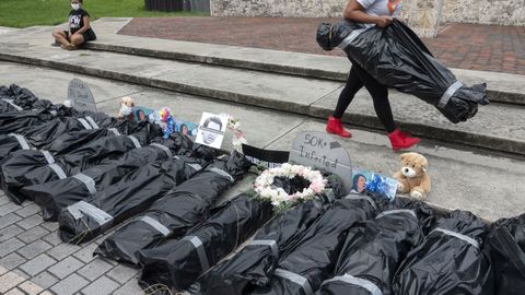 Un activista porta en Miami bolsas que simulan cuerpos de fallecidos por covid-19 en un acto de protesta