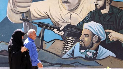 Un hombre y una mujer pasan junto a un mural de los Cuerpos de la Guardia Revolucionaria Isl�mica en Teher�n.