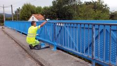 Un operario trabajando en el pintado de la pasarela en Valga
